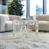 A mirrored round coffee table sits on a plush white rug in a living room setting, with two cream-colored armchairs and a large potted plant visible in the background. Anteprima dell’immagine prodotto