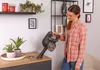 A woman is cleaning a wooden surface with a handheld vacuum cleaner. Voir les images du produit