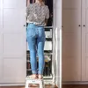 A person is standing on a white step stool in front of an open closet, reaching for items inside. Produktbild-Vorschau