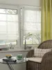 A cozy window seat area with a wicker chair, a glass table with a cup of tea and snacks, and Roman blinds on the window. Produktbild-Vorschau