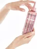 Hands holding a bottle of Kérastase hair product against a white background. Produktbild-Vorschau