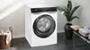 A Siemens washing machine is shown in a laundry room setting with a basket of clothes and a potted plant. Produktbild-Vorschau