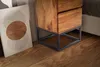 A wooden nightstand with a metal base sits on a wooden floor next to a piece of abstract art. Anteprima dell’immagine prodotto