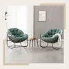 Two green papasan chairs with cushions are placed in a living room setting, with a small side table between them. A framed picture hangs on the wall behind the chairs. Produktbild-Vorschau
