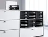 A white filing cabinet with black drawers and a black document tray on top, placed in an office setting near a window. Voir les images du produit