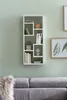 A white modern wall shelf with books and decorative items mounted on a light green wall above a gray sofa. Produktbild-Vorschau
