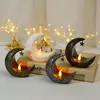 Four crescent moon-shaped candle holders with LED lights and hanging stars, arranged on a book. Produktbild-Vorschau