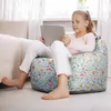 A young girl sits on a floral bean bag chair, holding a tablet. Náhľad obrázku produktu