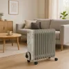 A white and gray oil-filled radiator is placed on a wooden floor in a living room, next to a sofa and a coffee table. Podgląd zdjęcia produktu