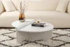 A white coffee table with a vase of branches and a book on it, placed on a patterned rug in front of a cream-colored sofa. Produktbild-Vorschau