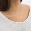 A close-up shot of a person wearing a delicate silver chain necklace. Produktbild-Vorschau