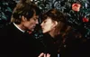 A man and a woman are looking at each other with their faces close together, with roses and foliage in the background. Produktbild-Vorschau