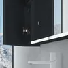 A close-up view of a black bathroom cabinet with an open door, revealing a hinge and a white shelf below. A white faucet is visible in the foreground. The background shows a snowy landscape through a window. Produktbild-Vorschau