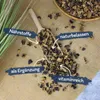 A wooden scoop filled with dried carob pieces, scattered on a burlap surface, with text overlays highlighting product features. Produktbild-Vorschau