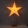A lit star-shaped lamp with a stand on a white surface against a dark gray background. Produktbild-Vorschau
