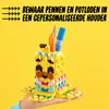 A hand holding a LEGO DOTS banana-shaped pencil holder filled with pens and pencils against a yellow background. Podgląd zdjęcia produktu