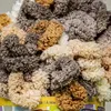 A close-up view of a pile of fluffy yarn in various neutral colors. Anteprima dell’immagine prodotto