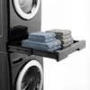 A close-up view of a black washing machine with a pull-out shelf holding folded towels. Podgląd zdjęcia produktu