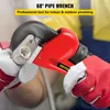 A person wearing gloves is using a red pipe wrench on a pipe fitting. Podgląd zdjęcia produktu
