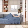 A woman is reading a book on a couch, covered by a blue blanket. Produktbild-Vorschau