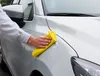 A person's hand is polishing a white car with a yellow cloth. Produktbild-Vorschau