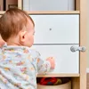 A baby is reaching for a drawer that has a child safety lock on it. Voir les images du produit