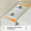 Close-up view of a white toilet seat attachment with installation hardware and orange arrows indicating movement, with text overlay. Produktbild-Vorschau