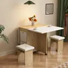 A dining set with a table and stools in a room with a plant and curtains. Produktbild-Vorschau
