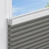 A close-up view of a gray honeycomb blind installed in a window frame, with a clear blue sky visible through the window. Produktbild-Vorschau