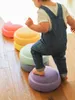A child in denim overalls is stepping on colorful balance stones. Anteprima dell’immagine prodotto