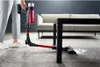 A person is using a cordless vacuum cleaner to clean up spilled white powder from a carpet in a living room setting, with a sofa and coffee table visible. Produktbild-Vorschau
