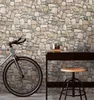 A bicycle is parked next to a dark wooden desk with a stool in front of it, against a stone-patterned wallpaper. Produktbild-Vorschau