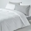 A close-up view of a neatly made bed with white and light gray bedding. Produktbild-Vorschau
