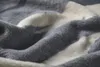 A close-up, textured view of a folded blanket with gray and white stripes. Produktbild-Vorschau