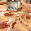 A miniature dollhouse kitchen scene with various accessories laid out on a wooden table. Náhľad obrázku produktu