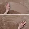 A hand touching a textured brown carpet. Produktbild-Vorschau