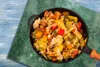 A close-up overhead view of a pan filled with a colorful vegetable stir-fry, placed on a textured green surface with a blue wooden background. Náhľad obrázku produktu