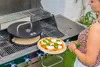 A woman is placing a pizza onto a grill with a pizza oven attachment. Náhľad obrázku produktu