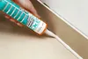 A hand is using a caulking gun to apply sealant along a corner where a wall meets a floor. Produktbild-Vorschau