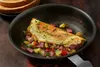 An omelet filled with corned beef and potatoes in a frying pan, with toast in the background. Produktbild-Vorschau