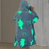 Kind trägt eine blaue Kapuzen-Decke mit im Dunkeln leuchtenden Dinosaurier- und Pfotenabdruck-Mustern, von hinten gesehen Produktbild-Vorschau
