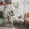 A mirrored round coffee table with decorative elements and a vase of greenery is placed between two chairs in a living room setting. Anteprima dell’immagine prodotto