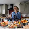 A woman in a kitchen is looking at a tablet, with various kitchen appliances and food items displayed around her. Voir les images du produit