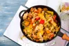 A close-up overhead shot of a pan filled with a colorful vegetable stir-fry, placed on a blue wooden surface with water droplets and a white orchid in the background. Náhľad obrázku produktu