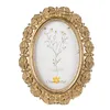 A gold-colored oval picture frame with a floral design and a picture of a plant inside. Anteprima dell’immagine prodotto