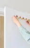A person is hanging an over-the-door hook rack with wooden pegs on a white door. Náhľad obrázku produktu