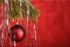 A close-up of a Christmas tree branch with a red ornament and silver tinsel against a red background. Produktbild-Vorschau