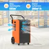 An orange and black commercial dehumidifier is shown in a warehouse setting with shelves of boxes in the background. Blue arrows indicate airflow from the device. Voir les images du produit
