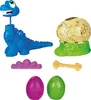 A collection of dinosaur-themed toys, including a blue dinosaur figure, a dinosaur egg, a bone, and a fossilized egg. Produktbild-Vorschau