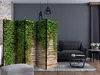 A room divider with an ivy wall design is placed in a living room setting next to a sofa. Náhľad obrázku produktu